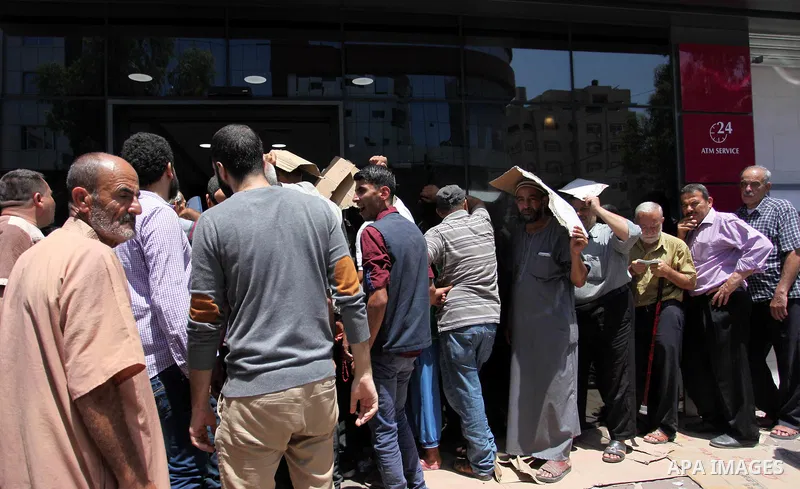 Palestinians of Social Affairs wait in front of Bank of Palestine to withdraw their financial aid in Gaza City on June 10, 2018. Photo by Mahmoud Ajour