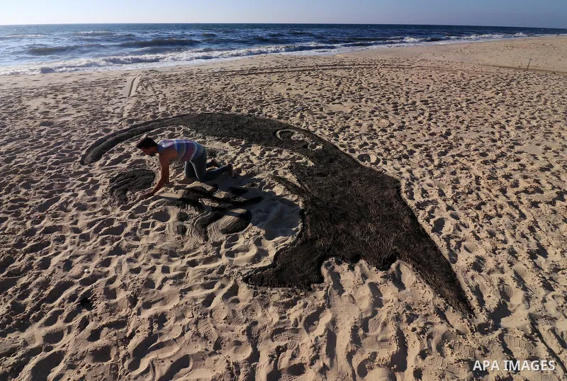 A Palestinian artist Osama Sbeata draws the portrait of Turkish President Recep Tayyip Erdogan on sand to celebrate the results of the Turkish presidential and parliamentary elections on Gaza Sea on June 26, 2018. Photo...