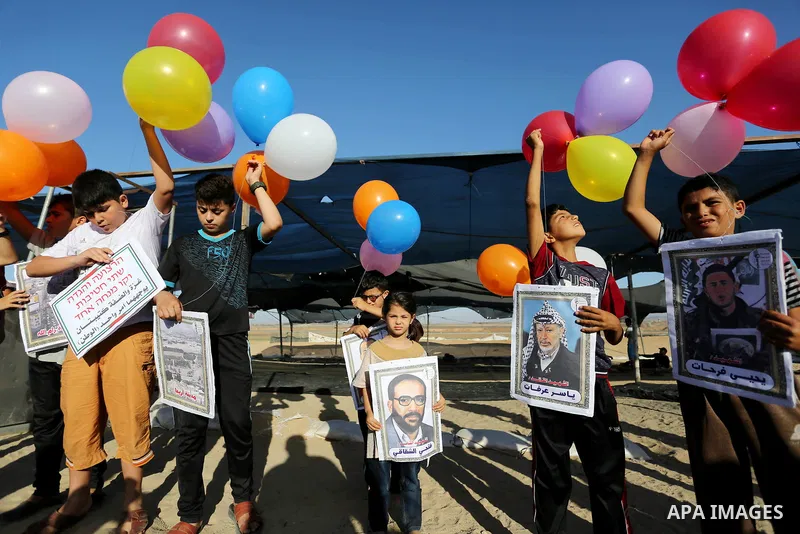 Palestinian children hold balloons before it be fly during a protest near tents at Gaza-Israel border, in Jabalia in the northern of Gaza Strip on June 27, 2018. Photo by Ashraf Amra
