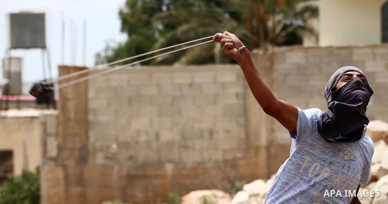 A Palestinian protester uses a slingshot to hurl stones towards Israeli troops during clashes following a demonstration against the expropriation of Palestinian land by Israel in the village of Kfar Qaddum, near Nablus,...
