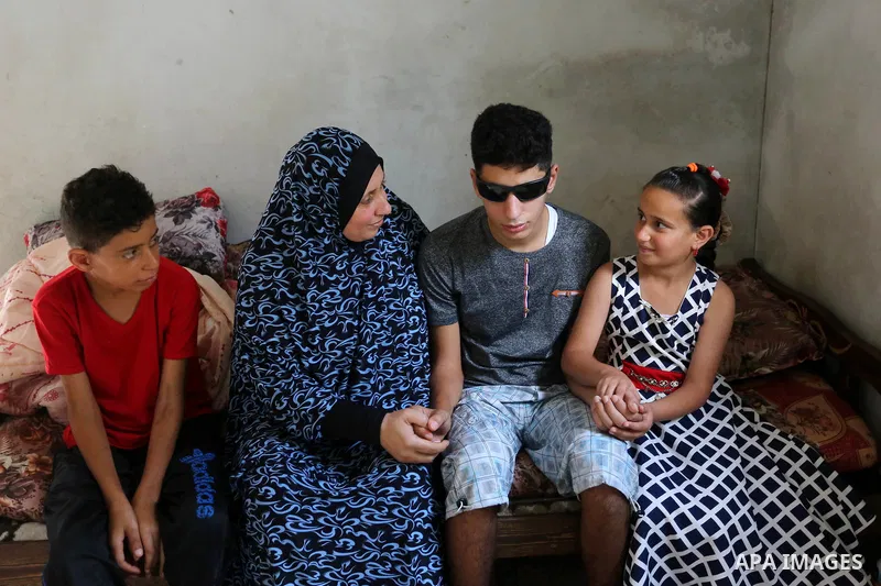 A Palestinian blind Saleh Ashour, 16, who lost his sight by Israeli troops during clashes at Gaza-Israel border, sits on a bed with his family their house in Nusseirat refugee camp in the center of Gaza Strip on July 1,...