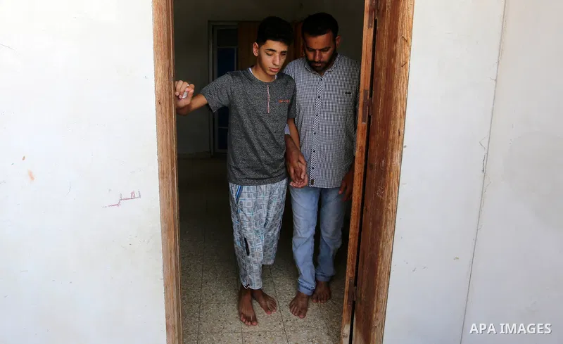 The father of Palestinian blind Saleh Ashour, 16, who lost his sight by Israeli troops during clashes at Gaza-Israel border, helps him to walk in Nusseirat refugee camp in the center of Gaza Strip on July 1, 2018. Photo...