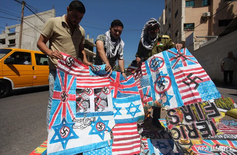 Palestinians burn an Israeli, British and U.S. flags during a protest to show solidarity with Palestinian prisoners held in Israeli jails, in front of Red cross office in Gaza city on July 2, 2018. Photo by Mahmoud Ajour