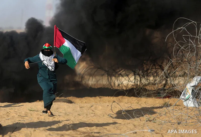 A Palestinian woman holds the national flag during clashes with Israeli troops in tents protest where Palestinian demand the right to return to their homeland at the Israel-Gaza border, in Khan Younis in the southern Gaz...