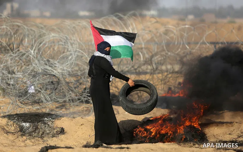 A Palestinian woman holds the national flag as she burns tires during clashes with Israeli troops in tents protest where Palestinian demand the right to return to their homeland at the Israel-Gaza border, in Khan Younis...