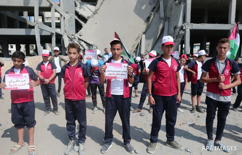 Palestinian boys take part in a protest against the killing of Palestinian children, in front of the building that was damaged in an Israeli airstrike on the Gaza City, on July 17, 2018. Photo by Ashraf Amra