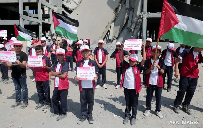 Palestinian boys take part in a protest against the killing of Palestinian children, in front of the building that was damaged in an Israeli airstrike on the Gaza City, on July 17, 2018. Photo by Ashraf Amra