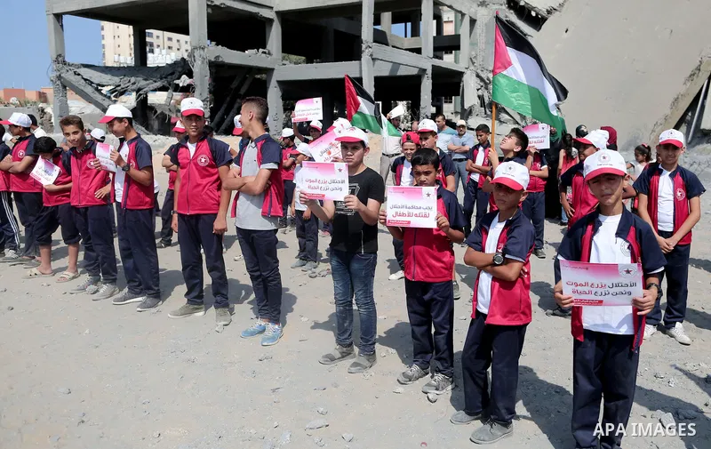 Palestinian boys take part in a protest against the killing of Palestinian children, in front of the building that was damaged in an Israeli airstrike on the Gaza City, on July 17, 2018. Photo by Ashraf Amra