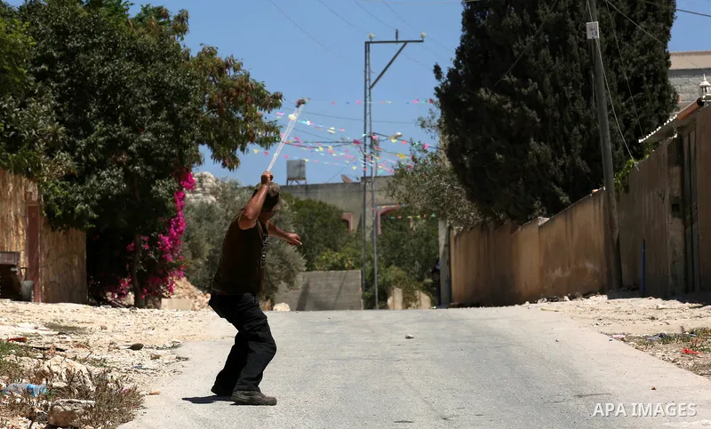 A masked Palestinian uses a slingshot to hurl stones towards Israeli troops during clashes following a demonstration against the expropriation of Palestinian land by Israel in the village of Kfar Qaddum, near Nablus, in...