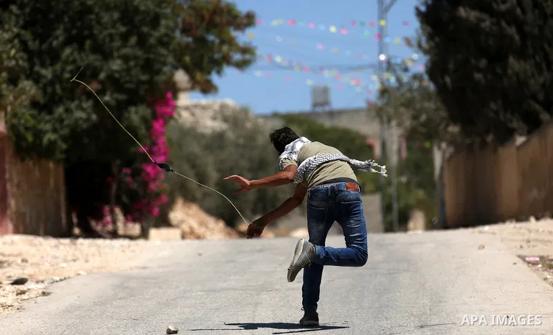 A masked Palestinian uses a slingshot to hurl stones towards Israeli troops during clashes following a demonstration against the expropriation of Palestinian land by Israel in the village of Kfar Qaddum, near Nablus, in...