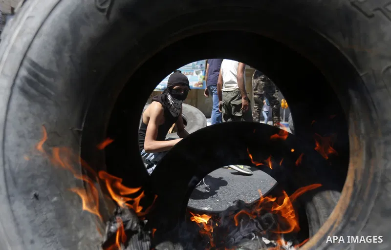 Palestinian protesters burn tyres during clashes following a demonstration, in the West Bank city of Hebron, on July 27, 2018. Photo by Wisam Hashlamoun