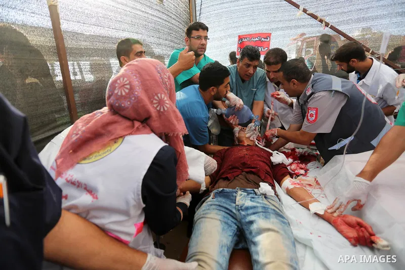 Palestinian medics help a wounded Palestinian protester after he was shot by Israeli troops during clashes in tents protest where Palestinians demand the right to return to their homeland at the Israel-Gaza border, in Kh...