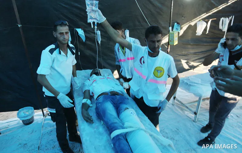 Palestinian medics help a wounded Palestinian protester after he was shot by Israeli troops during clashes in tents protest where Palestinians demand the right to return to their homeland at the Israel-Gaza border, in Kh...