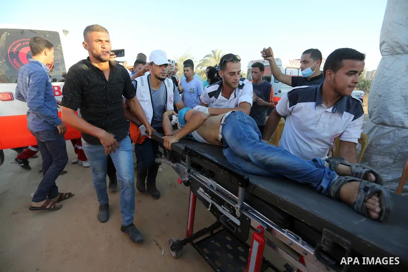Palestinian medics help a wounded Palestinian protester after he was shot by Israeli troops during clashes in tents protest where Palestinians demand the right to return to their homeland at the Israel-Gaza border, in Kh...