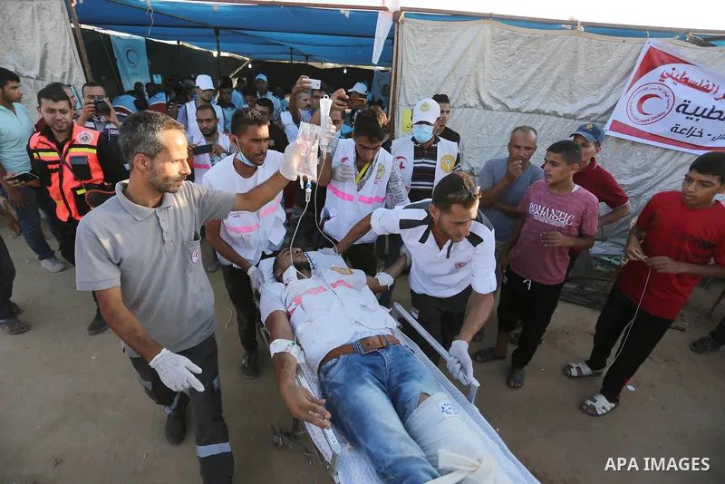 Palestinian medics help a wounded Palestinian protester after he was shot by Israeli troops during clashes in tents protest where Palestinians demand the right to return to their homeland at the Israel-Gaza border, in Kh...
