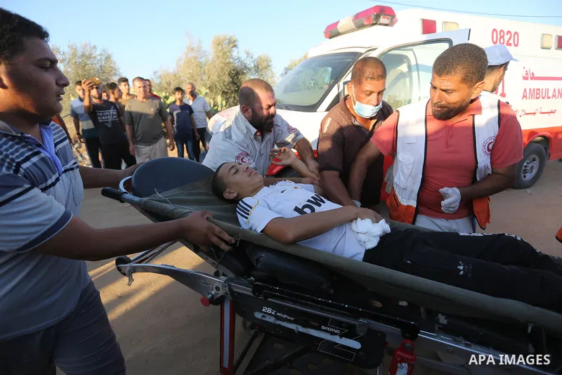 Palestinian medics help a wounded Palestinian protester after he was shot by Israeli troops during clashes in tents protest where Palestinians demand the right to return to their homeland at the Israel-Gaza border, in Kh...