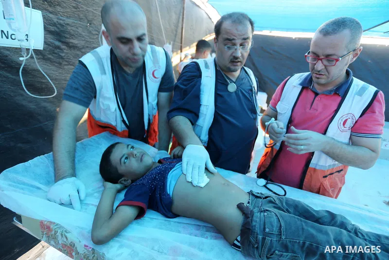 Palestinian medics help a wounded Palestinian protester after he was shot by Israeli troops during clashes in tents protest where Palestinians demand the right to return to their homeland at the Israel-Gaza border, in Kh...