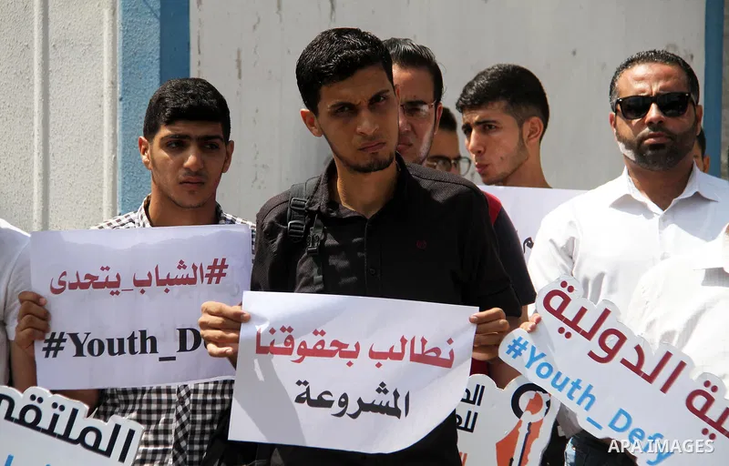 Palestinian youths hold banners during a protest to demand their rights in front of United Nations Development Programme office (UNDP) in Gaza City on August 12, 2018. Photo by Mahmoud Ajour