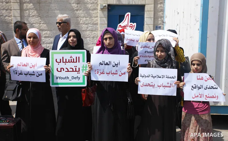 Palestinian youths hold banners during a protest to demand their rights in front of United Nations Development Programme office (UNDP) in Gaza City on August 12, 2018. Photo by Mahmoud Ajour
