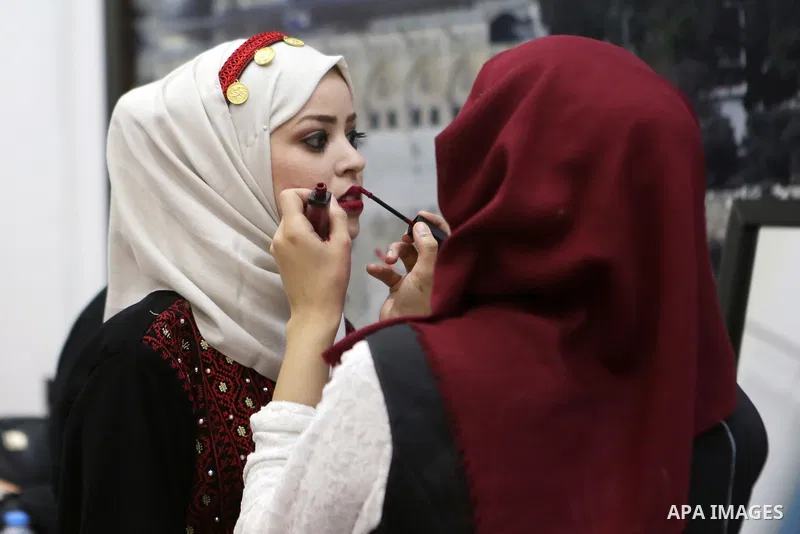 A Palestinian bride puts on her make-up during a mass wedding celebration held under the patronage of Palestinian President Mahmoud Abbas, in the West Bank city of Ramallah on August 18, 2018. Photo by Shadi Hatem