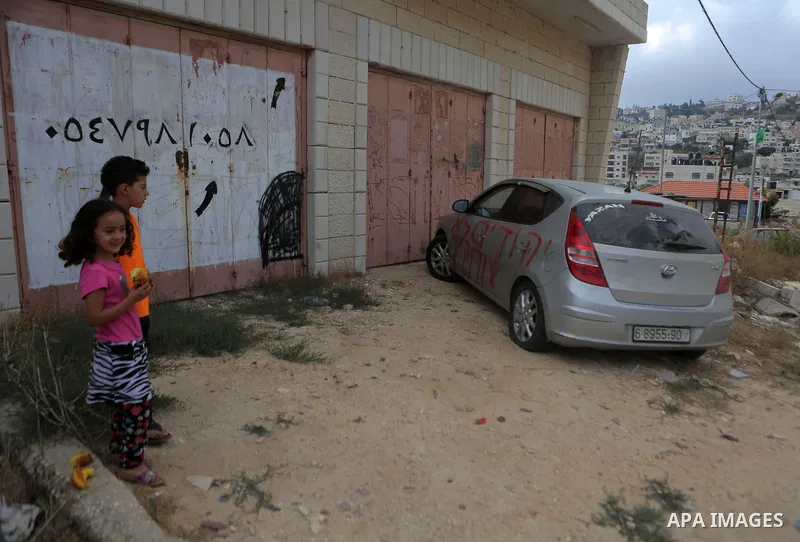 Palestinian children look at a car that was sprayed with racist slogans that read in Hebrew "Jews will not be silent", in the West Bank town of Singel north of Ramallah, on August 27, 2018. Photo by Shadi Hatem