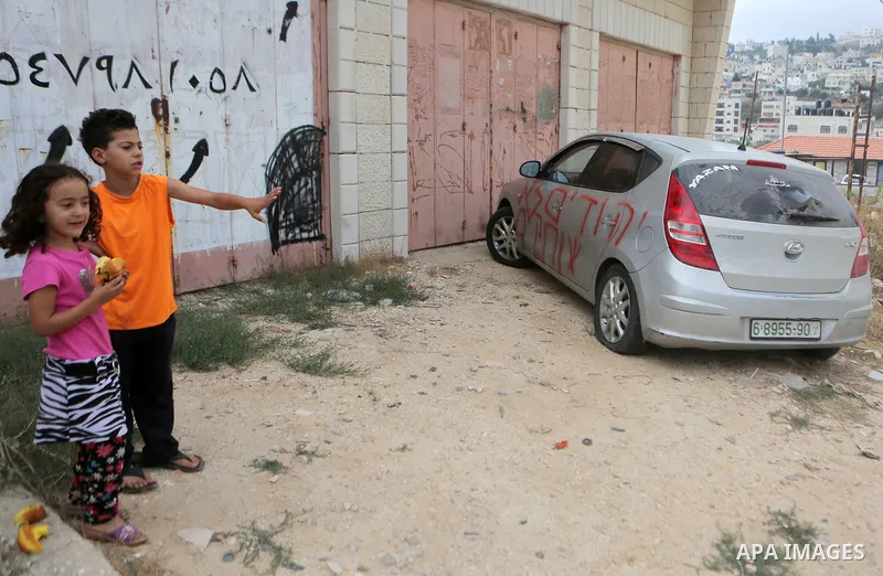 Palestinian children look at a car that was sprayed with racist slogans that read in Hebrew "Jews will not be silent", in the West Bank town of Singel north of Ramallah, on August 27, 2018. Photo by Shadi Hatem