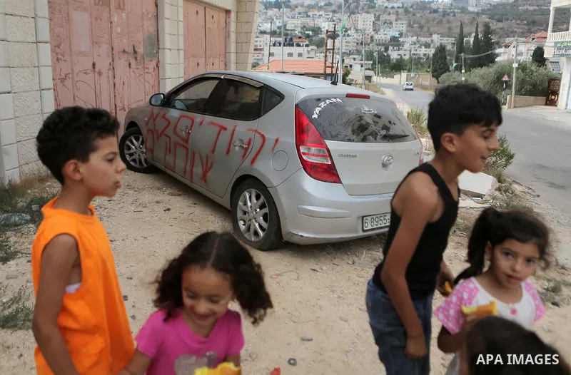 Palestinian children look at a car that was sprayed with racist slogans that read in Hebrew "Jews will not be silent", in the West Bank town of Singel north of Ramallah, on August 27, 2018. Photo by Shadi Hatem