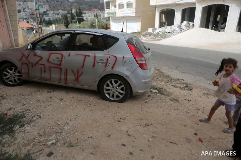Palestinian children look at a car that was sprayed with racist slogans that read in Hebrew "Jews will not be silent", in the West Bank town of Singel north of Ramallah, on August 27, 2018. Photo by Shadi Hatem