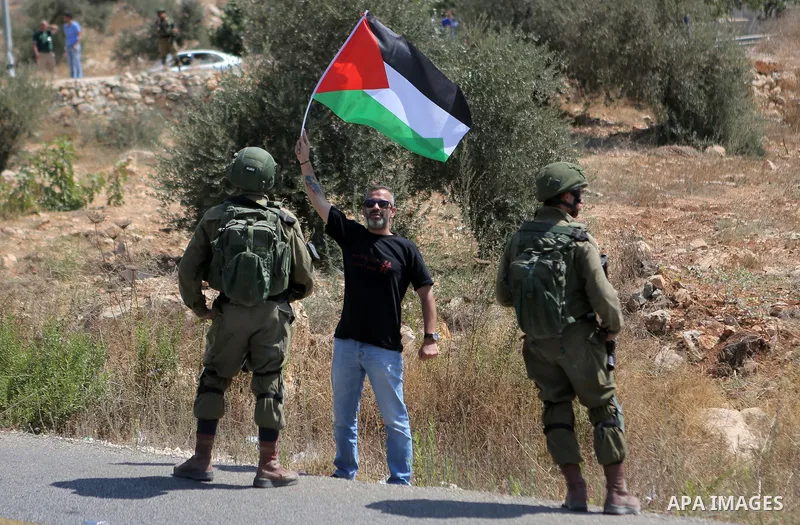 A Palestinian man holds the national flag in front of Israeli border policemen during a protest in the village of Ras Karkar, near the West Bank city of Ramallah on August 29, 2018. Photo by Shadi Hatem