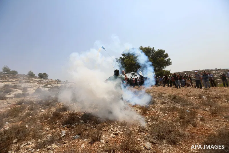 A Palestinian protester throws back a tear gas canister fired by Israeli border policemen during a protest against Israeli settlement construction, in the village of Ras Karkar, near the West Bank city of Ramallah on Aug...