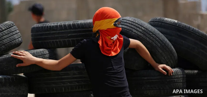 A masked Palestinian protester stands next to tires during clashes with Israeli forces following a weekly demonstration against the expropriation of Palestinian land by Israel in the village of Kfar Qaddum, near the West...