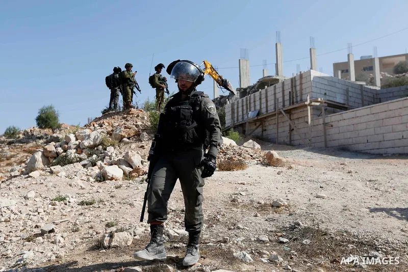 Israeli border policemen stand guard as Israeli bulldozer demolishes four houses owned by Palestinian families which Israeli authorities said it was built without a permit, in the West Bank village of Walajeh, near Bethl...
