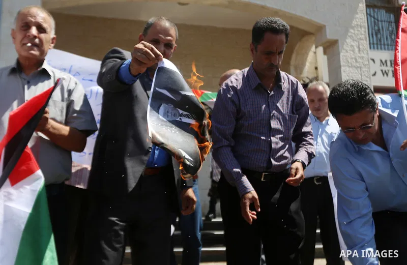 Palestinian protesters burn a picture of US president Donald Trump and Israeli Prime Minister Benjamin Netanyahu during a demonstration to protest against the US president's cuts to aid for Palestinians, outside an offic...