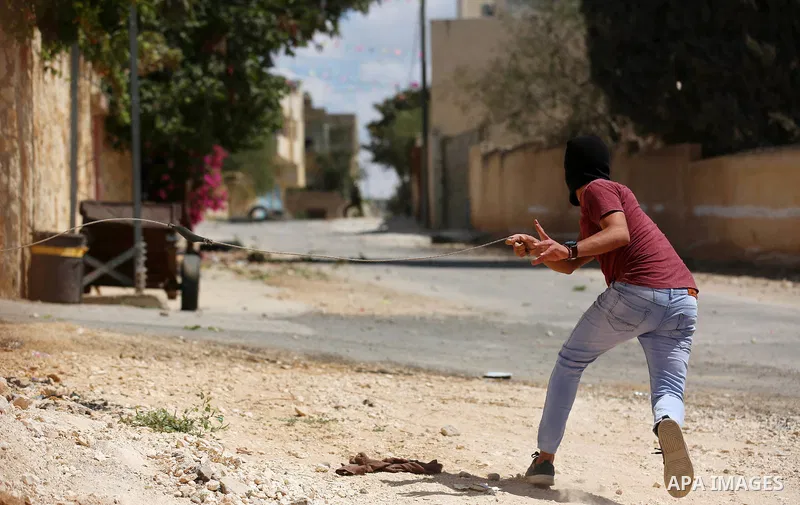 A Palestinian protester uses a slingshot to hurl stones towards Israeli forces during clashes following a weekly demonstration against the expropriation of Palestinian land by Israel in the village of Kfar Qaddum, near t...