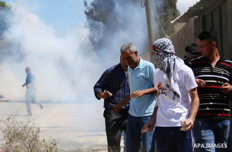 Palestinian protesters take cover from a tear gas canister fired by Israeli forces during clashes following a weekly demonstration against the expropriation of Palestinian land by Israel in the village of Kfar Qaddum, ne...