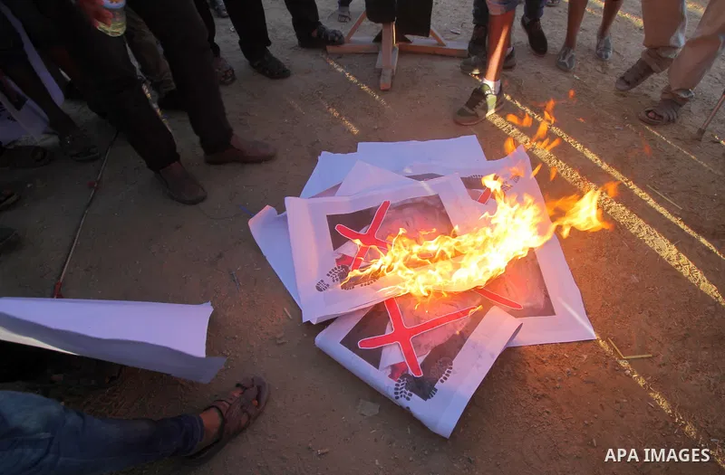 Palestinian protesters burn posters depicting US President Donald Trump during clashes with Israeli troops in tents protest where Palestinians demand the right to return to their homeland at the Israel-Gaza border, in ea...