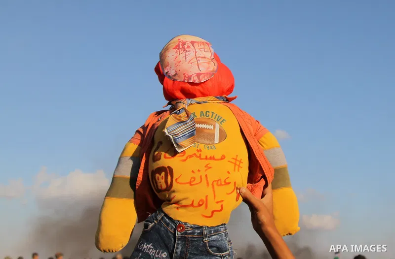 A Palestinian protester holds up a doll wearing a mask depicting US President Donald Trump's face covered with blood and a shirt with an Arabic slogan reading "Continuing in spite of Trump", during clashes with Israeli t...