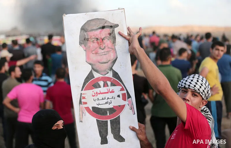 Palestinian protesters hold a cartoon sign depicting US President Donald Trump with a caption below reading in Arabic "we are returning in spite of you, Trump", during clashes with Israeli troops in tents protest where P...