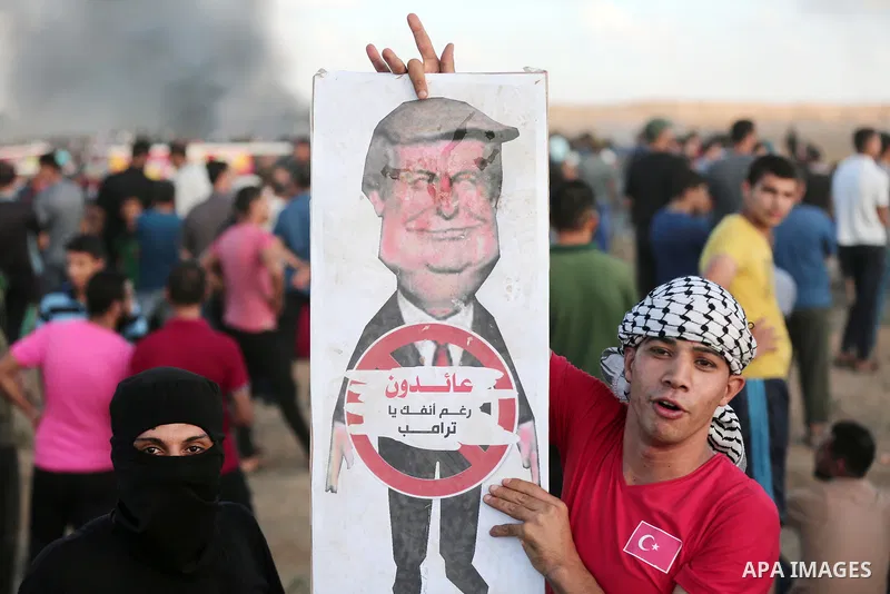 Palestinian protesters hold a cartoon sign depicting US President Donald Trump with a caption below reading in Arabic "we are returning in spite of you, Trump", during clashes with Israeli troops in tents protest where P...