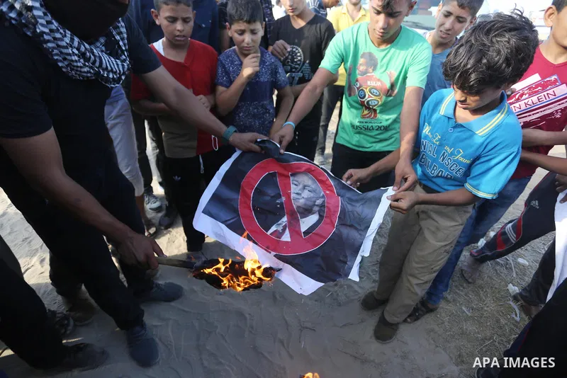 Palestinian protesters burn posters depicting US President Donald Trump during clashes with Israeli troops in tents protest where Palestinians demand the right to return to their homeland at the Israel-Gaza border, in Kh...