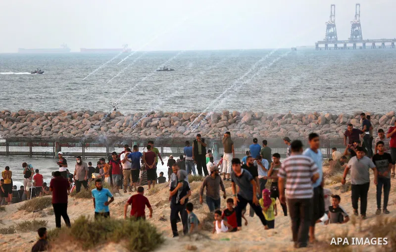 Palestinian protesters take cover from tear gas canisters are fired by Israeli troops during a demonstration against the Israeli blockade on Gaza Strip, along the Gaza sea barrier on the maritime border with Israel near...