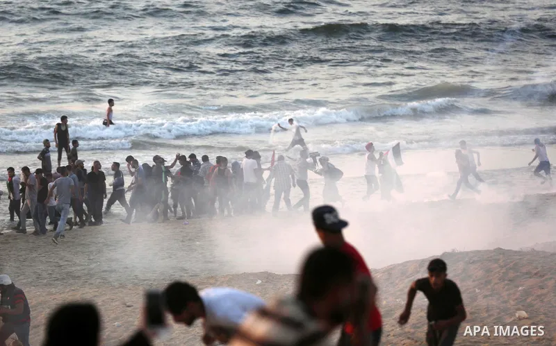 Palestinian protesters take cover from tear gas canisters are fired by Israeli troops during a demonstration against the Israeli blockade on Gaza Strip, along the Gaza sea barrier on the maritime border with Israel near...