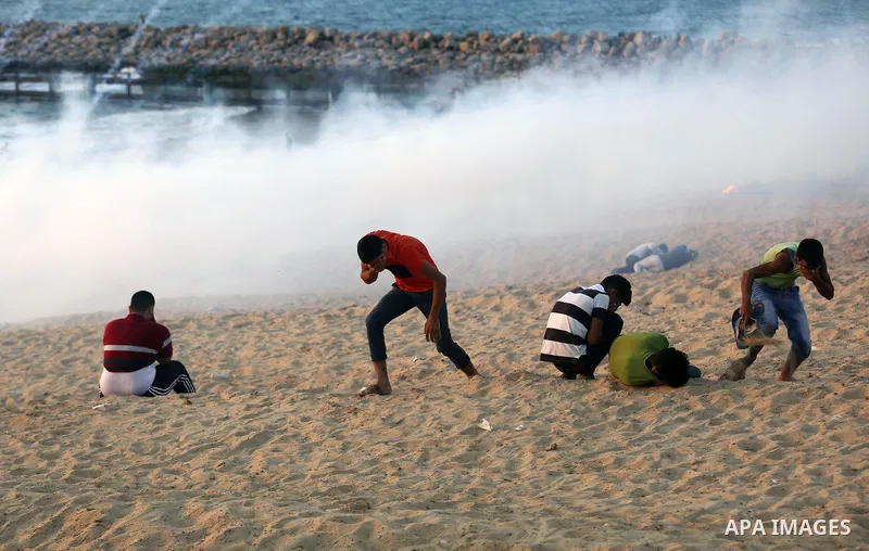 Palestinian protesters take cover from tear gas canisters are fired by Israeli troops during a demonstration against the Israeli blockade on Gaza Strip, along the Gaza sea barrier on the maritime border with Israel near...