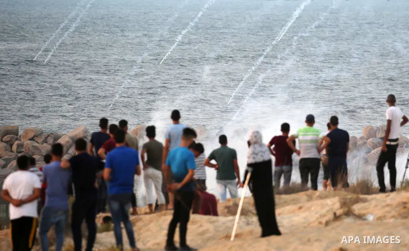 Palestinian protesters take cover from tear gas canisters are fired by Israeli troops during a demonstration against the Israeli blockade on Gaza Strip, along the Gaza sea barrier on the maritime border with Israel near...