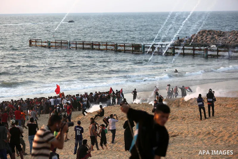Palestinian protesters take cover from tear gas canisters are fired by Israeli troops during a demonstration against the Israeli blockade on Gaza Strip, along the Gaza sea barrier on the maritime border with Israel near...