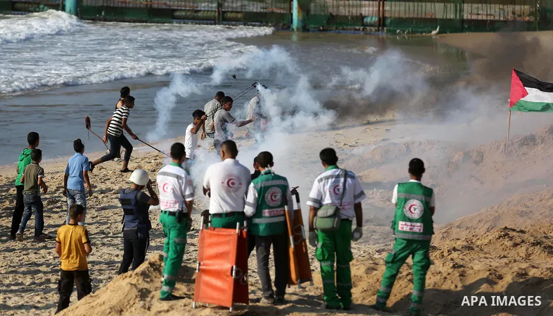 Palestinian protesters take cover from tear gas canisters are fired by Israeli troops during a demonstration against the Israeli blockade on Gaza Strip, along the Gaza sea barrier on the maritime border with Israel near...