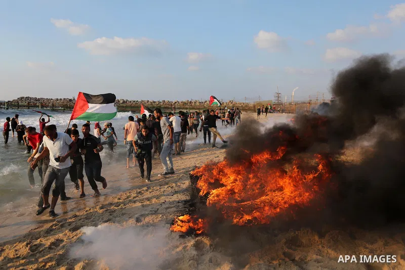 Palestinian protesters take cover from tear gas canisters are fired by Israeli troops during a demonstration against the Israeli blockade on Gaza Strip, along the Gaza sea barrier on the maritime border with Israel near...