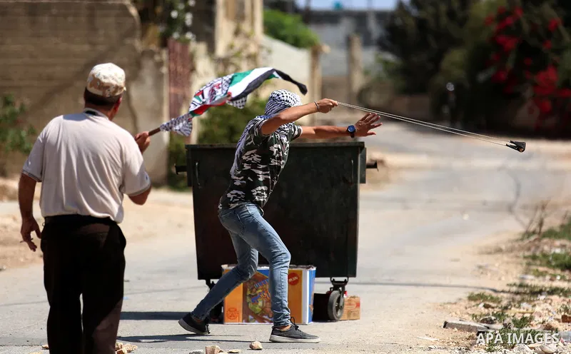 A masked Palestinian protester uses a slingshot to hurl stones towards Israeli forces during clashes following a weekly demonstration against the expropriation of Palestinian land by Israel in the village of Kfar Qaddum,...