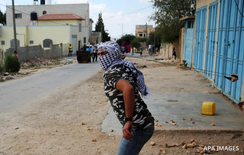 A masked Palestinian protester uses a slingshot to hurl stones towards Israeli forces during clashes following a weekly demonstration against the expropriation of Palestinian land by Israel in the village of Kfar Qaddum,...