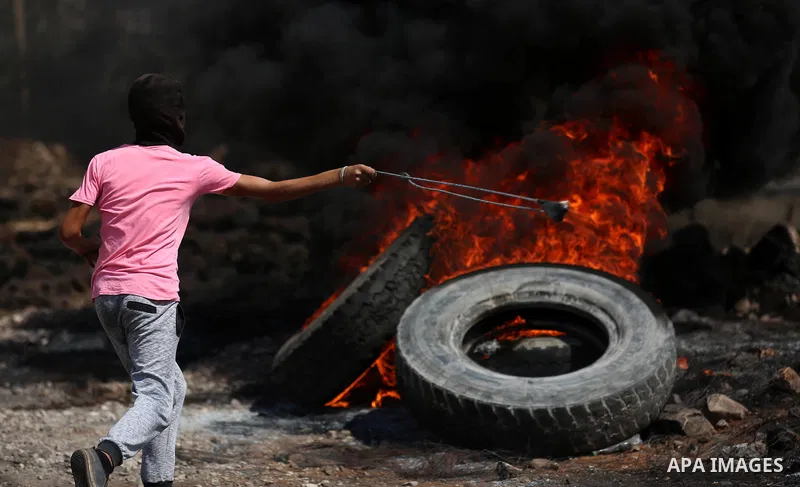 A masked Palestinian protester uses a slingshot to hurl stones towards Israeli forces during clashes following a weekly demonstration against the expropriation of Palestinian land by Israel in the village of Kfar Qaddum,...